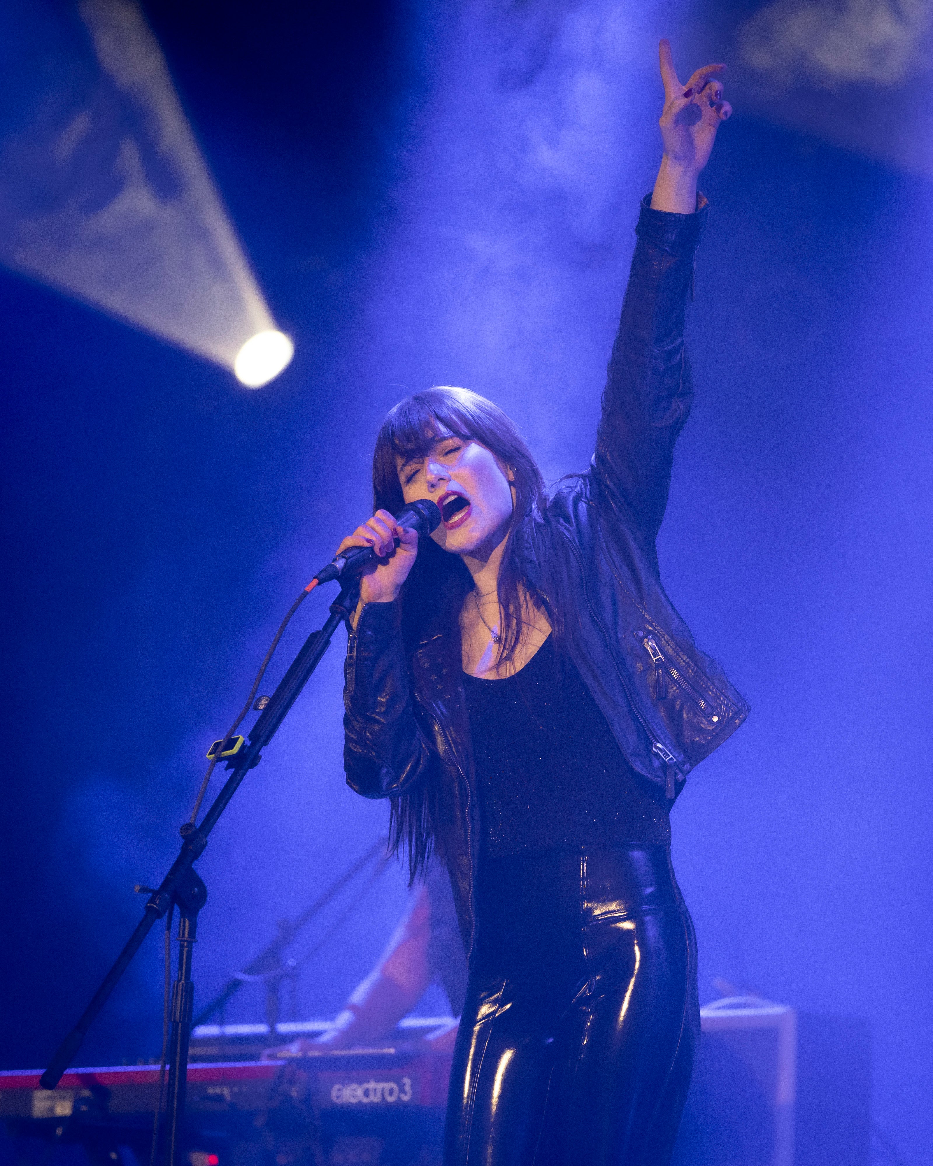 Sydney Irving on stage with microphone and raised hand, surrounded by blue lighting and smoke.